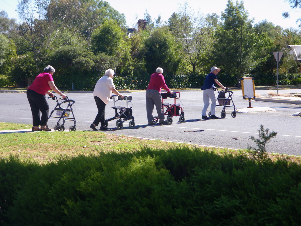 Four people walking across the street using assistive devices